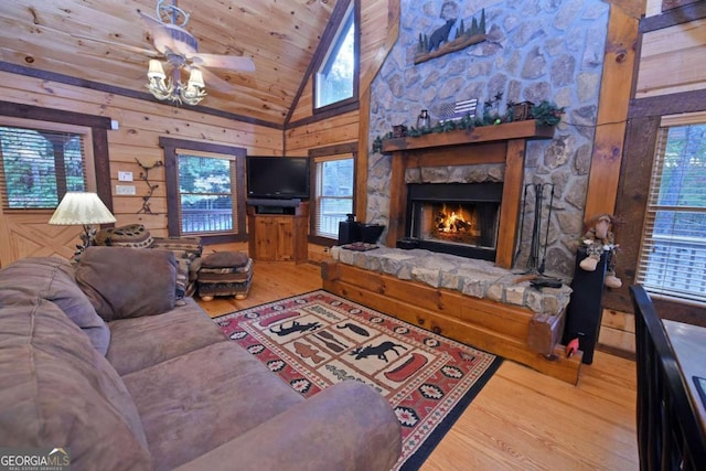 living room with a healthy amount of sunlight, a stone fireplace, wood walls, and ceiling fan