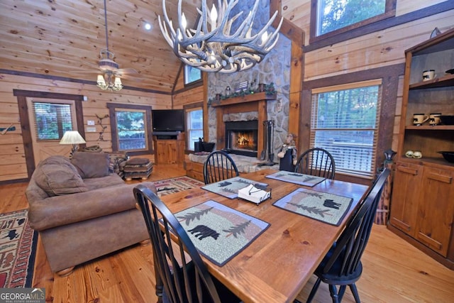 dining room featuring light wood-type flooring, a fireplace, wooden walls, and a wealth of natural light