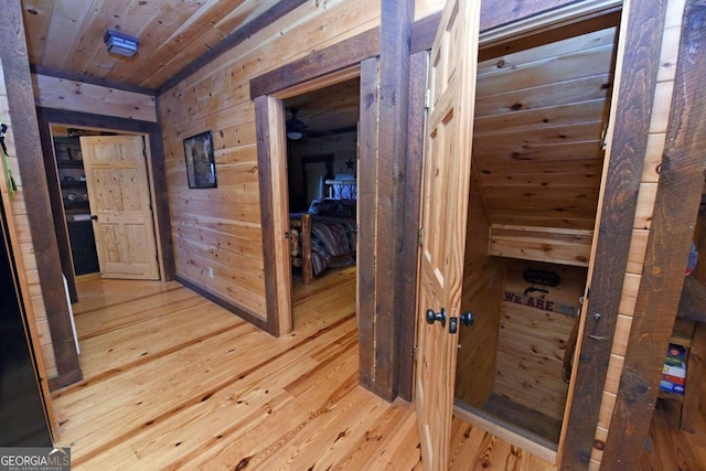 hallway with light hardwood / wood-style flooring, wood walls, and wooden ceiling