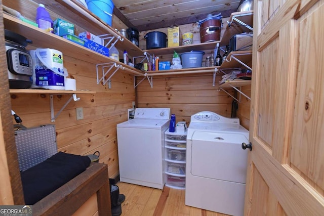 washroom with light hardwood / wood-style flooring, wood walls, and washing machine and dryer