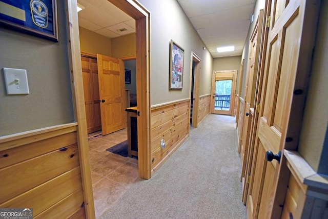 hallway featuring light colored carpet and wooden walls