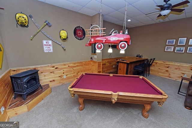 rec room featuring a wood stove, a drop ceiling, ceiling fan, pool table, and wooden walls