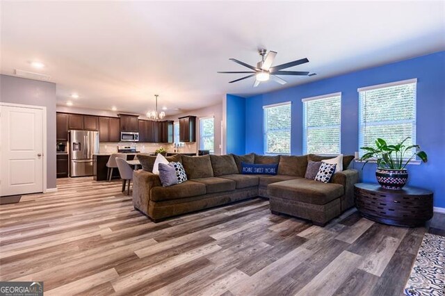 living room featuring ceiling fan with notable chandelier and light hardwood / wood-style floors