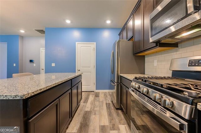 kitchen with light hardwood / wood-style floors, a kitchen island, appliances with stainless steel finishes, dark brown cabinetry, and light stone countertops