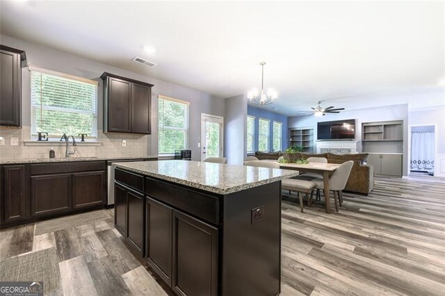 kitchen featuring decorative backsplash, light hardwood / wood-style floors, ceiling fan with notable chandelier, a kitchen island, and pendant lighting