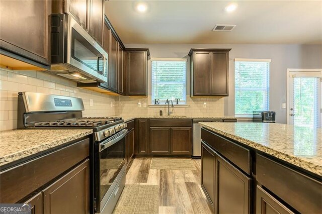 kitchen with light stone counters, stainless steel appliances, light hardwood / wood-style floors, and a wealth of natural light