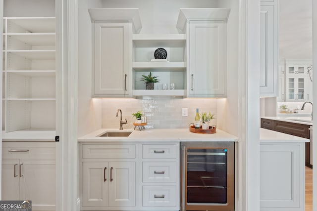 bar featuring sink, wine cooler, white cabinetry, and backsplash