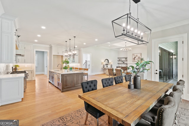 dining room featuring light wood-type flooring, crown molding, sink, and a chandelier