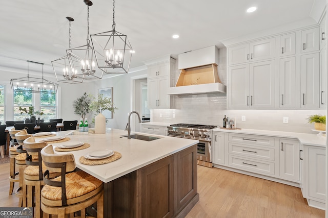 kitchen with premium range hood, white cabinets, a center island with sink, and double oven range