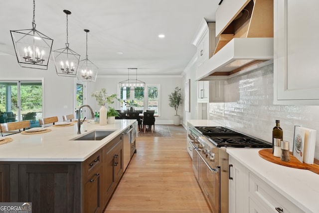 kitchen featuring light wood-type flooring, a kitchen island with sink, white cabinets, appliances with stainless steel finishes, and premium range hood