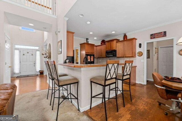 kitchen featuring black appliances, kitchen peninsula, ornamental molding, and hardwood / wood-style flooring