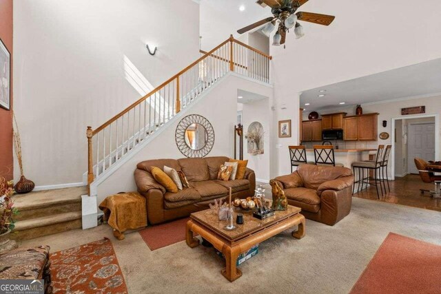 living room with a skylight, ceiling fan, a high ceiling, hardwood / wood-style floors, and ornamental molding