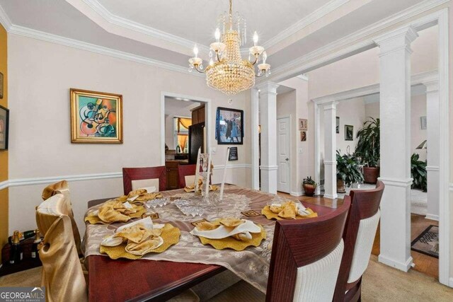 carpeted dining room with a chandelier, decorative columns, a tray ceiling, and ornamental molding