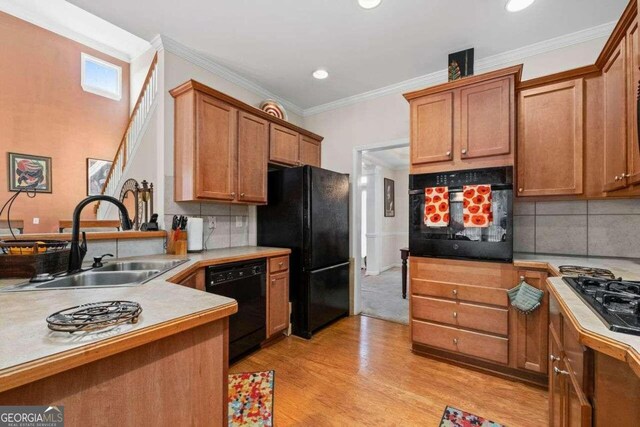 kitchen with decorative backsplash, ornamental molding, sink, black appliances, and light hardwood / wood-style floors