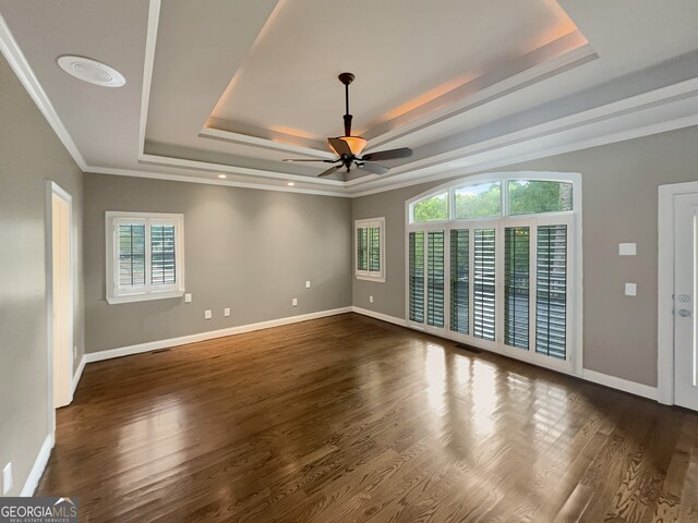 empty room with a raised ceiling, crown molding, ceiling fan, and dark wood-type flooring