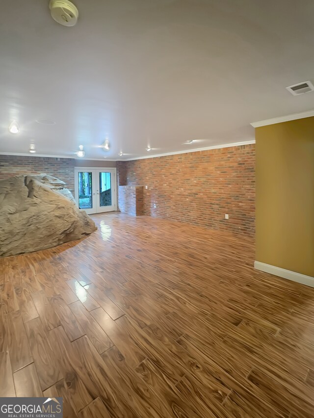 unfurnished living room featuring hardwood / wood-style flooring, ornamental molding, and brick wall