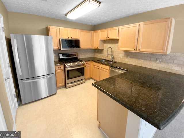 kitchen with dark stone counters, kitchen peninsula, appliances with stainless steel finishes, and sink