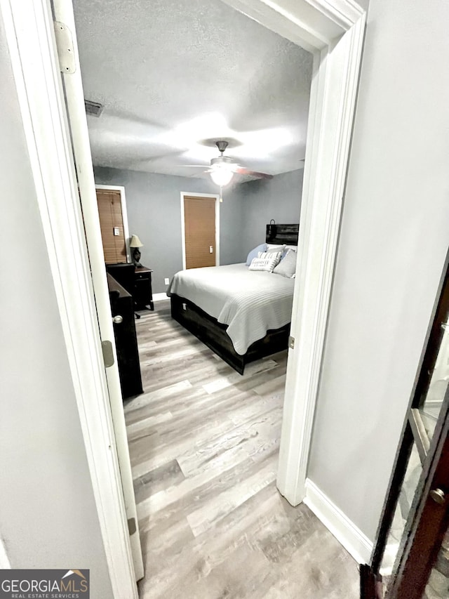 bedroom with ceiling fan, a textured ceiling, and light wood-type flooring