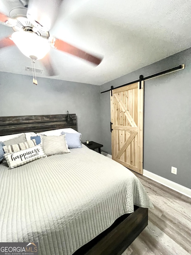 bedroom with a barn door, hardwood / wood-style floors, and ceiling fan