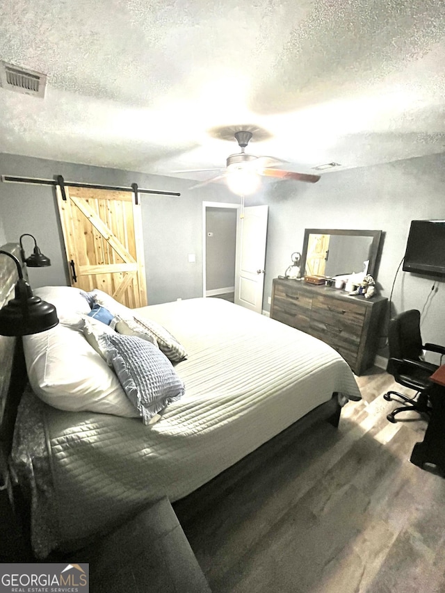 bedroom with ceiling fan, a textured ceiling, hardwood / wood-style floors, and a barn door