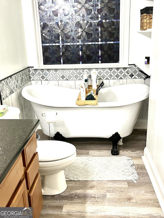 bathroom with vanity, a bath, hardwood / wood-style flooring, tile walls, and toilet