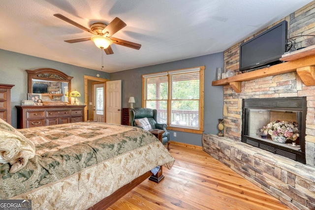 bedroom with light wood-type flooring, a stone fireplace, and ceiling fan