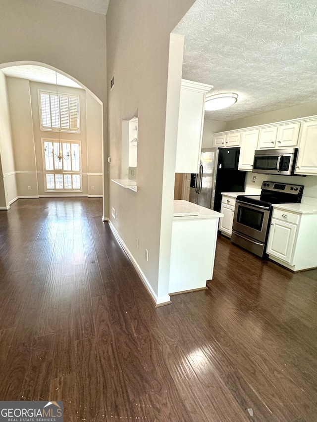 kitchen with appliances with stainless steel finishes, a textured ceiling, dark hardwood / wood-style flooring, and white cabinets