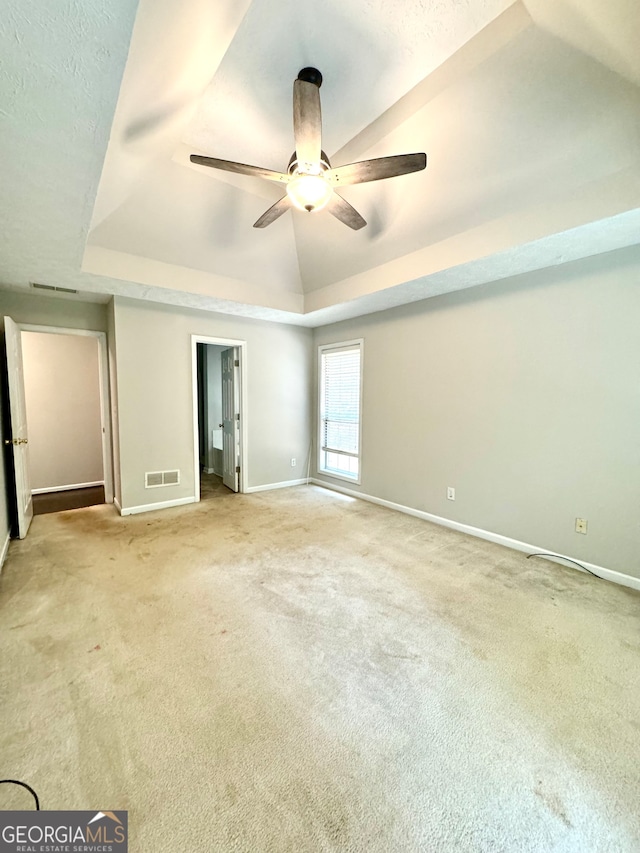 unfurnished bedroom featuring ceiling fan, carpet floors, a tray ceiling, and vaulted ceiling