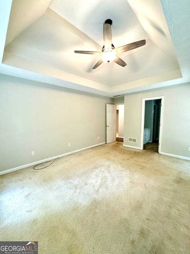 unfurnished bedroom with ceiling fan, a raised ceiling, and light carpet