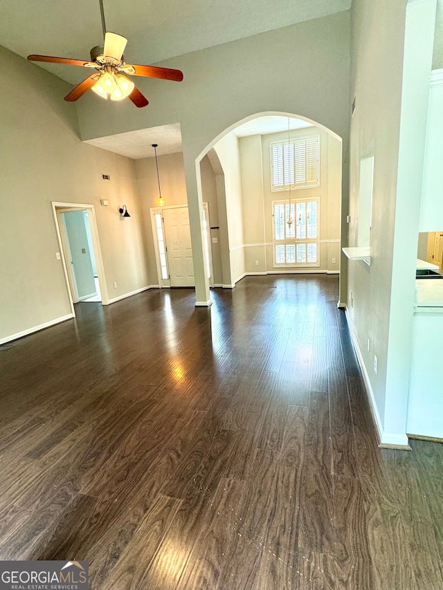 unfurnished living room featuring ceiling fan, dark wood-type flooring, and a high ceiling