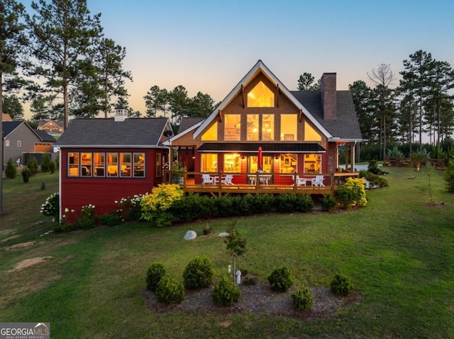 back house at dusk with a lawn and a wooden deck