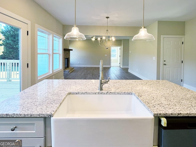 kitchen featuring light stone counters, dark wood-style flooring, a fireplace, a sink, and pendant lighting