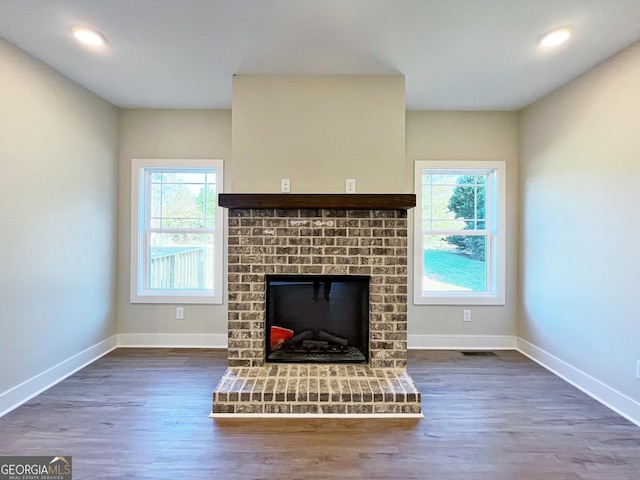 unfurnished living room with a healthy amount of sunlight, a brick fireplace, baseboards, and wood finished floors