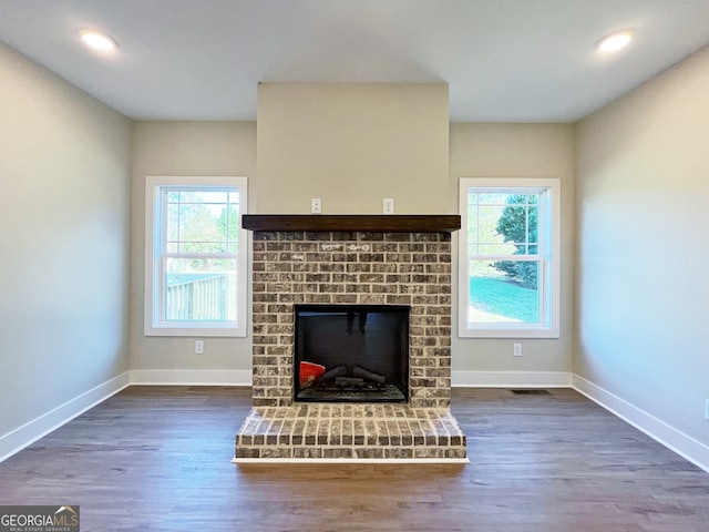 unfurnished living room with a brick fireplace, a healthy amount of sunlight, and dark hardwood / wood-style flooring