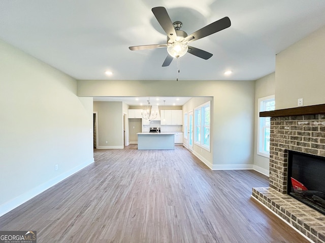 unfurnished living room featuring baseboards, wood finished floors, ceiling fan with notable chandelier, a fireplace, and recessed lighting