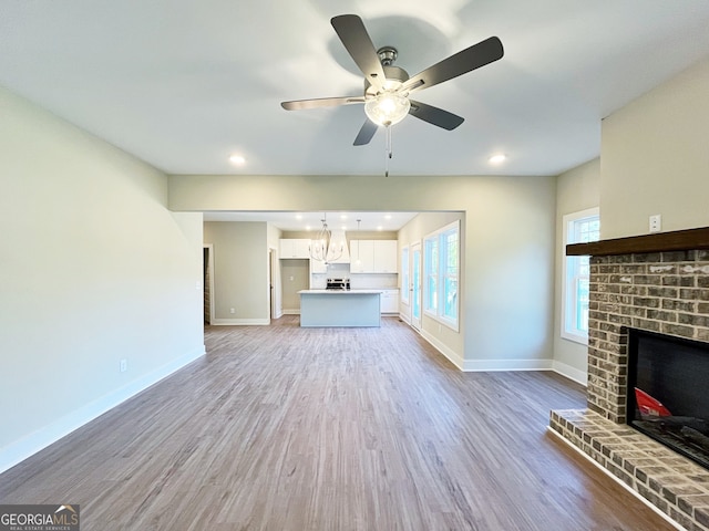 unfurnished living room featuring a brick fireplace, wood-type flooring, and ceiling fan with notable chandelier