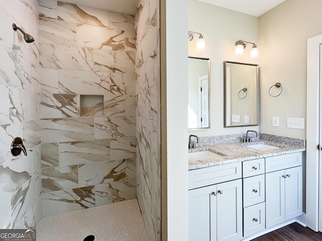 full bath featuring tiled shower, a sink, and double vanity