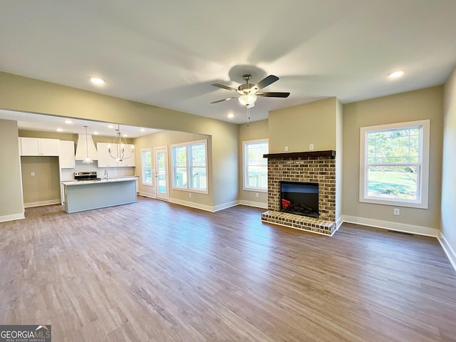 unfurnished living room featuring recessed lighting, ceiling fan with notable chandelier, dark wood-type flooring, a fireplace, and baseboards