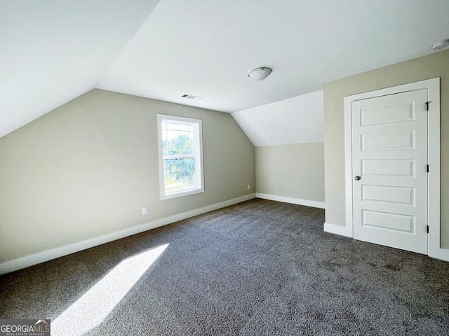 additional living space with visible vents, baseboards, vaulted ceiling, and dark colored carpet