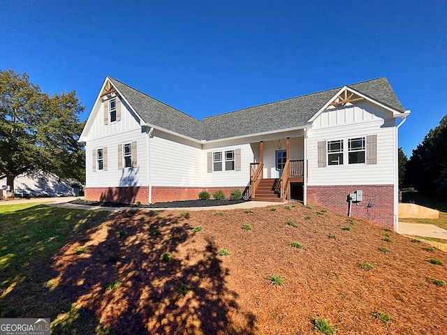 modern farmhouse featuring covered porch, roof with shingles, board and batten siding, and a front yard