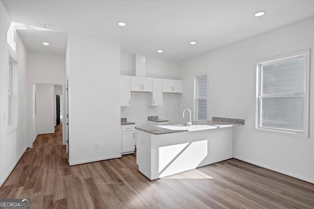 kitchen featuring kitchen peninsula, light hardwood / wood-style floors, white cabinetry, and light stone counters