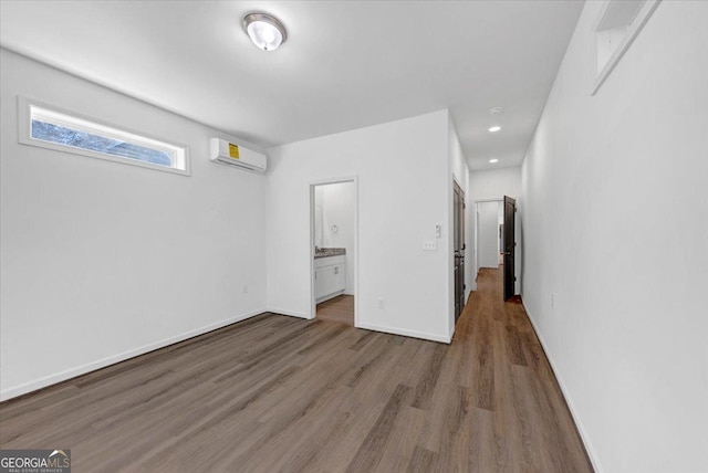 unfurnished bedroom with connected bathroom, wood-type flooring, and a wall mounted air conditioner