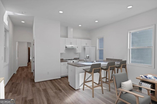 kitchen with hardwood / wood-style flooring, a breakfast bar, white cabinetry, and white fridge with ice dispenser