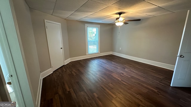 empty room with a drop ceiling, ceiling fan, and dark wood-type flooring