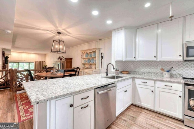 kitchen featuring appliances with stainless steel finishes, white cabinetry, kitchen peninsula, wood walls, and sink