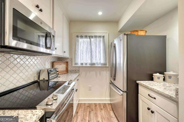 kitchen featuring appliances with stainless steel finishes, light wood-type flooring, light stone countertops, and white cabinets