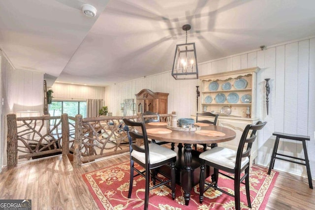 dining area with light hardwood / wood-style flooring, wood walls, and a chandelier