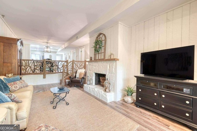 living room with light wood-type flooring, a fireplace, and wooden walls