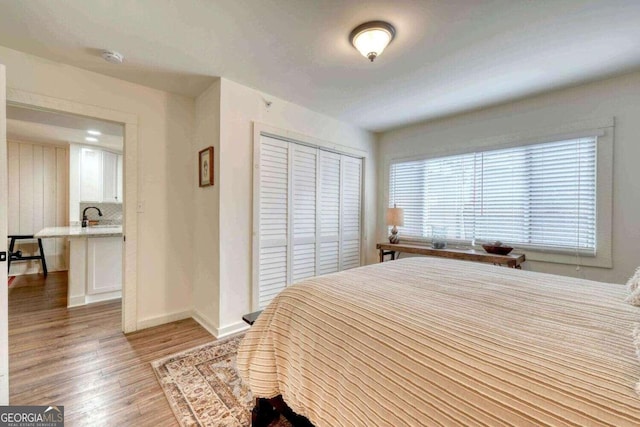 bedroom with a sink, light wood finished floors, a closet, and baseboards