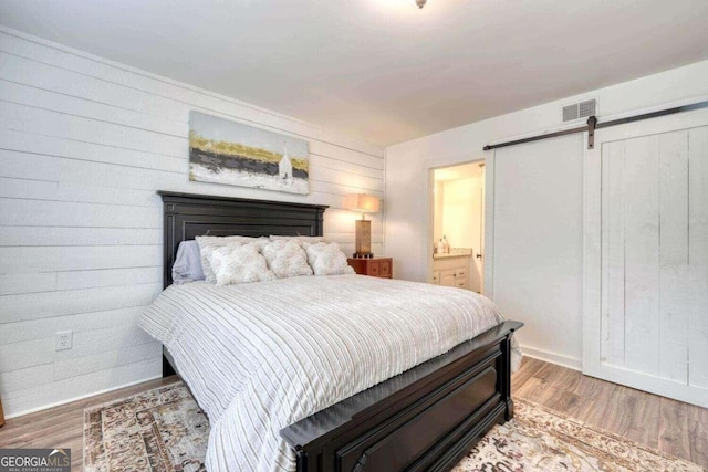 bedroom featuring ensuite bath, wood walls, hardwood / wood-style flooring, and a barn door